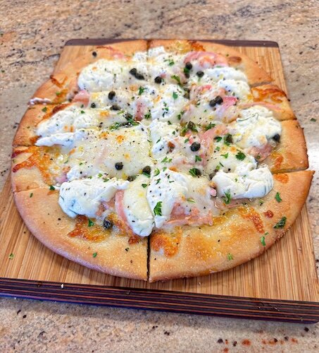 The lox pizza has an olive oil base, everything bagel seasoning, and fresh dill. It’s then topped with cold smoked salmon, pickled red onion, capers, and a lemon cream cheese ricotta.