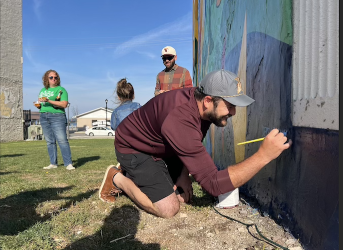 Artist Derek Brennan signs the mural during the dedication ceremony Oct. 30.