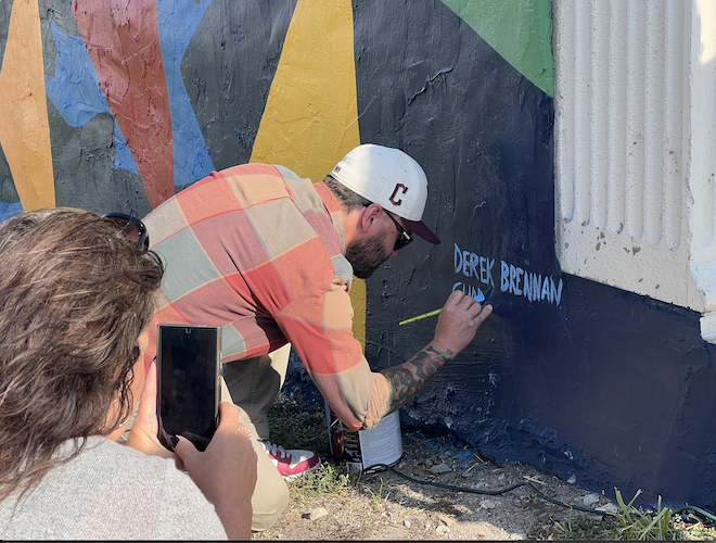 Artist Chad Fedorovich signs the mural during the dedication ceremony Oct. 30.