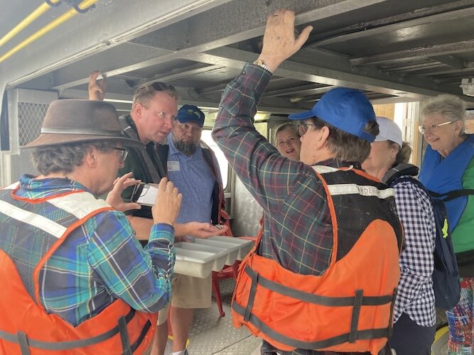 Zak Slagle, fisheries biologist at the Sandusky Fisheries Research Station, holds a container of young fish and points out what types of fish they are to a group aboard one of the station's research boats.